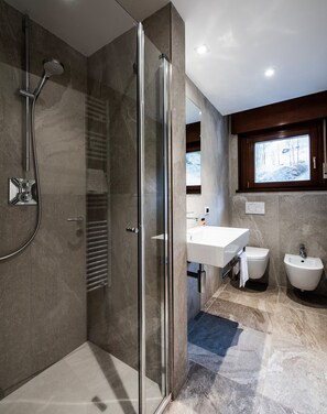 A modern bathroom with a glass-enclosed shower, a vanity with a bidet, and a large window above the sink.