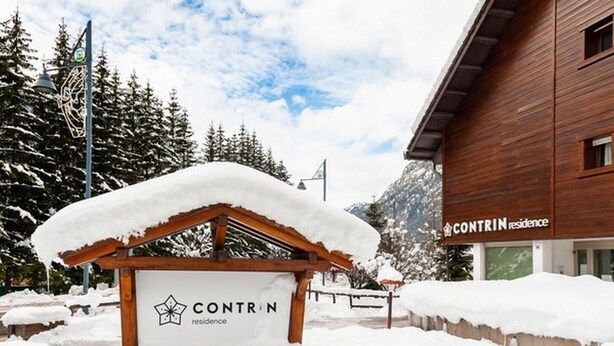 Ein Schild der CONTRIN Residences zeigt ein mit Schnee bedecktes Dach und eine Holzkonstruktion.