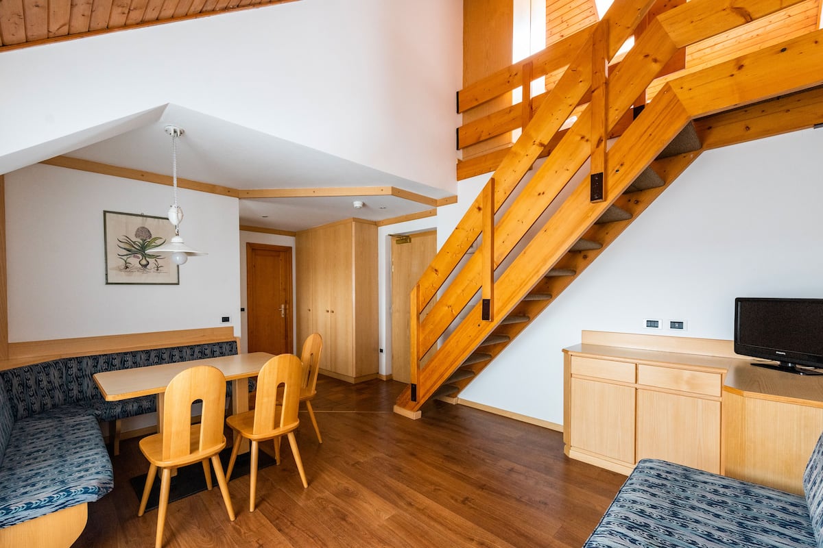 A modern interior with a wooden staircase, a dining area with a bench, and a television on a wooden cabinet.