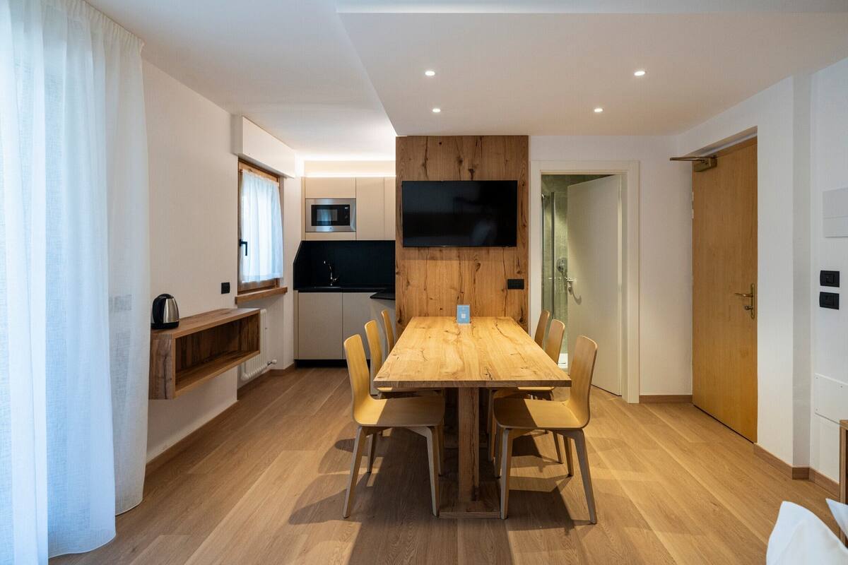 A compact living space with a dining area, kitchenette, and a television mounted on the wall.