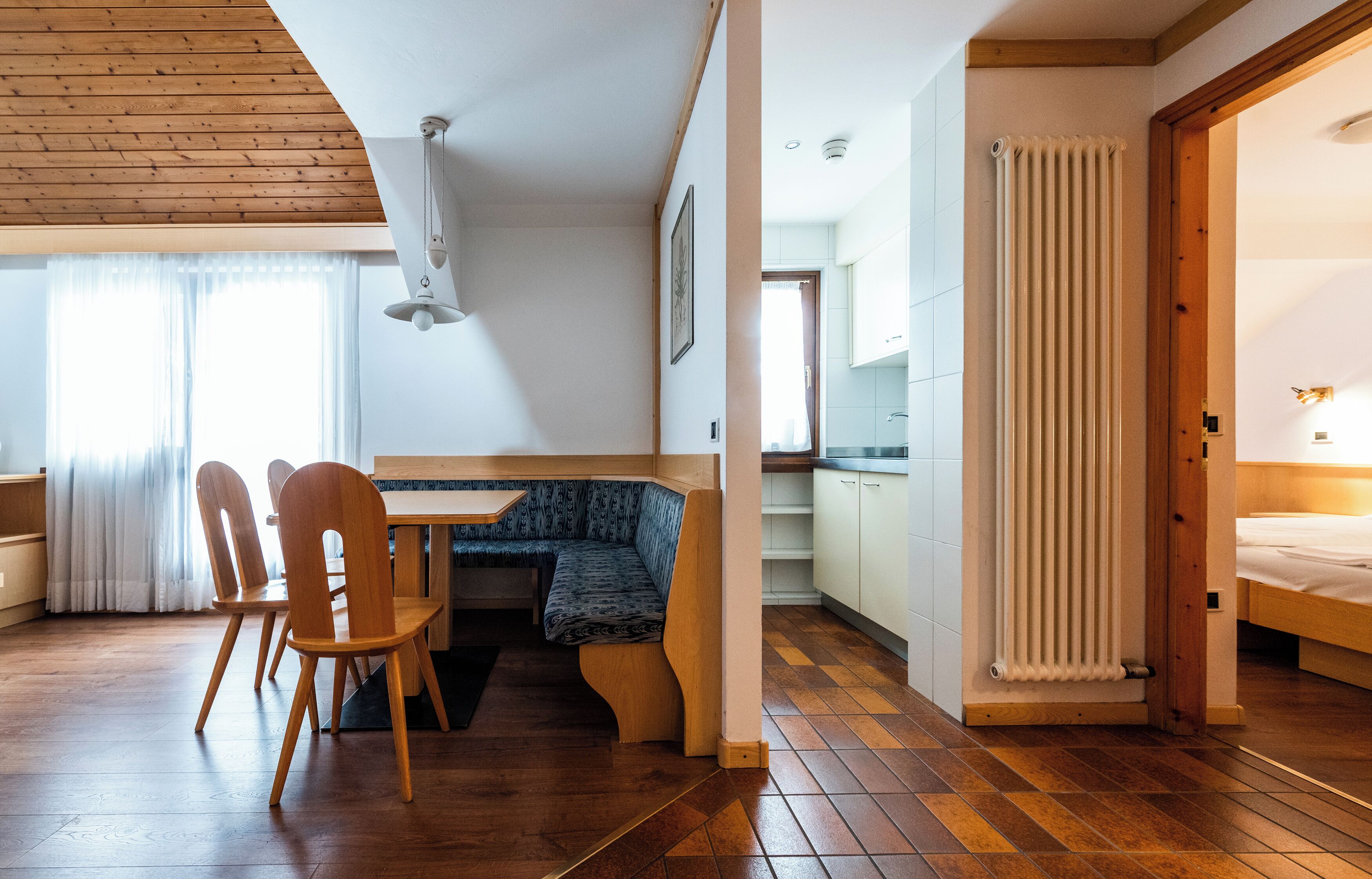 Una habitación acogedora con techo de madera, una mesa de comedor con sillas, un banco, un radiador y una cama.
