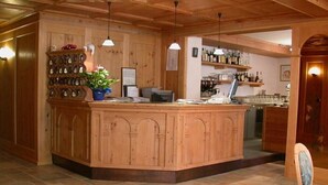 A wooden reception desk with a potted plant, a telephone, and various items on the counter. - Corona (CARANO)