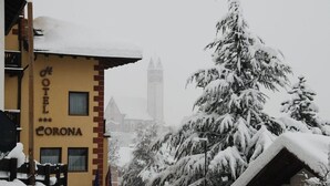 A snow-covered hotel named "HOTEL CORONA" with a visible clock tower in the background. - Corona (CARANO)