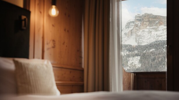 A wooden room with a bed and a window overlooking a mountain. - Diana Dolomites  (Badia)