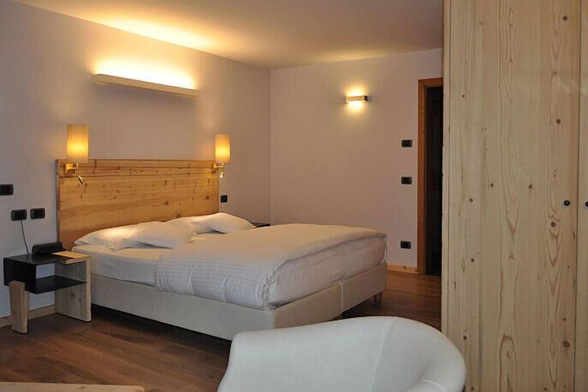 A bedroom with a wooden headboard, a bedside table, a chair, and two wall-mounted lights.