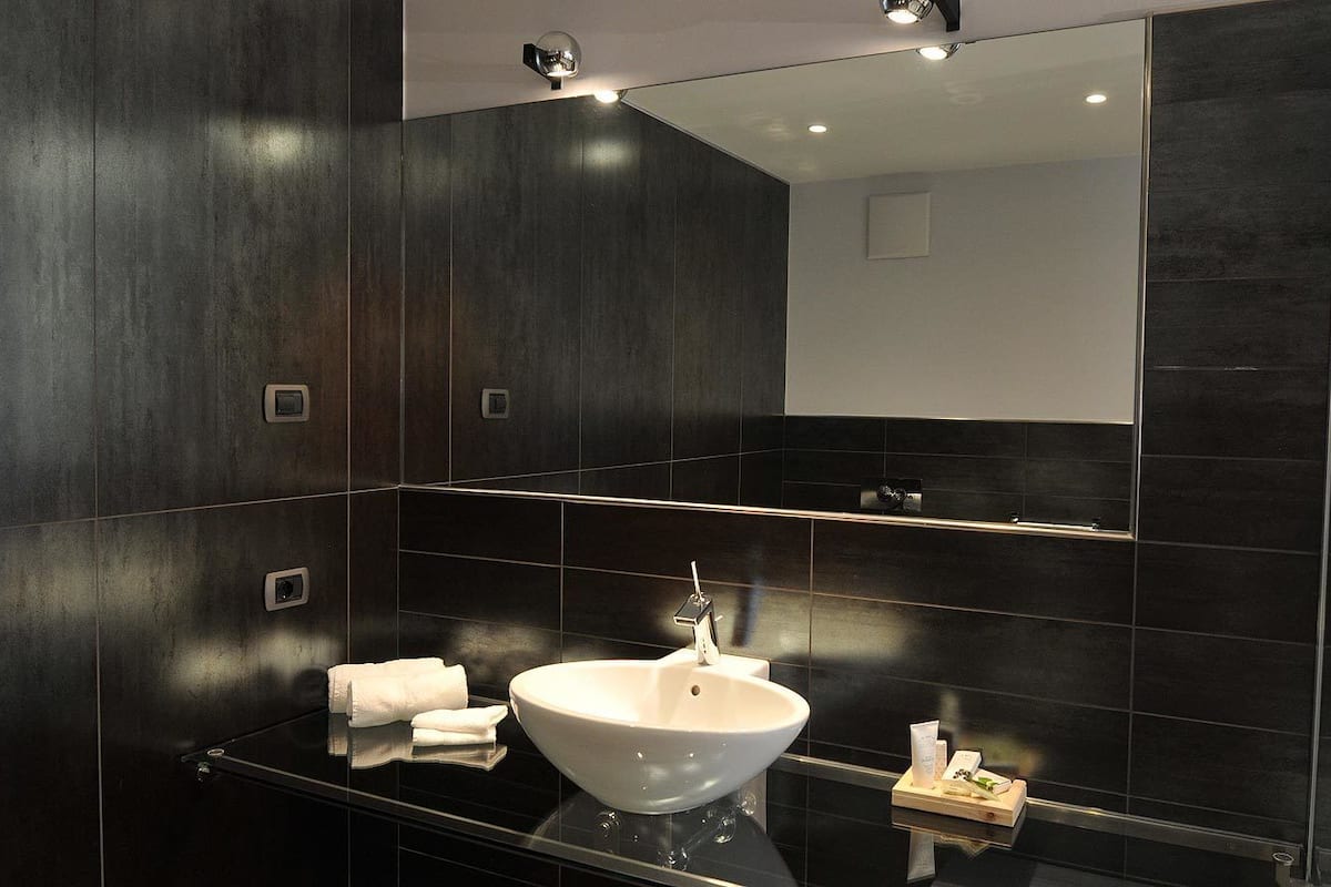 A modern bathroom with dark wood paneling, a white sink, and a large mirror.