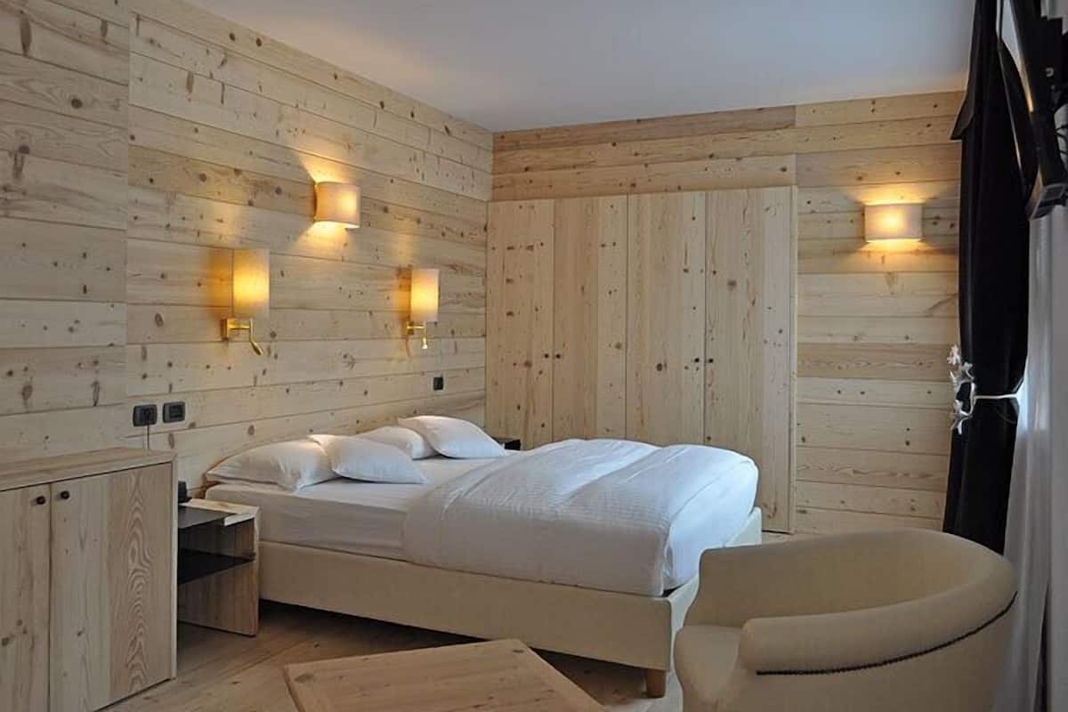 A wooden-paneled room with a bed, bedside table, chair, and wall-mounted lights.