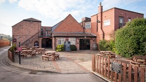 A brick building with a patio area featuring wooden tables and benches. - Unicorn, Gunthorpe by Marston's Inns (Nottingham)