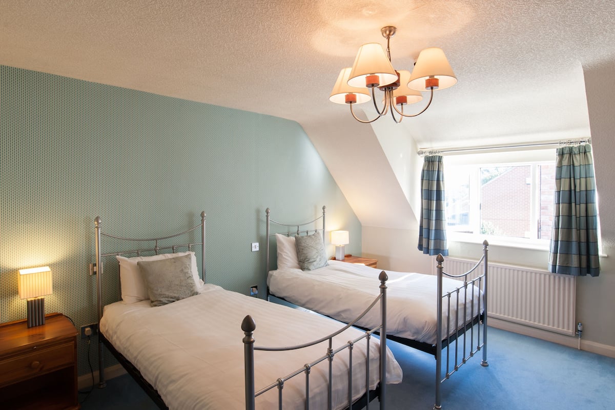 A bedroom with two beds, a chandelier, a window with curtains, and a radiator.