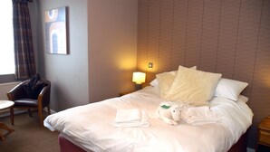 A hotel room with a neatly made bed, a chair, a lamp, and a wall with a geometric pattern. - Unicorn, Gunthorpe by Marston's Inns (Nottingham)
