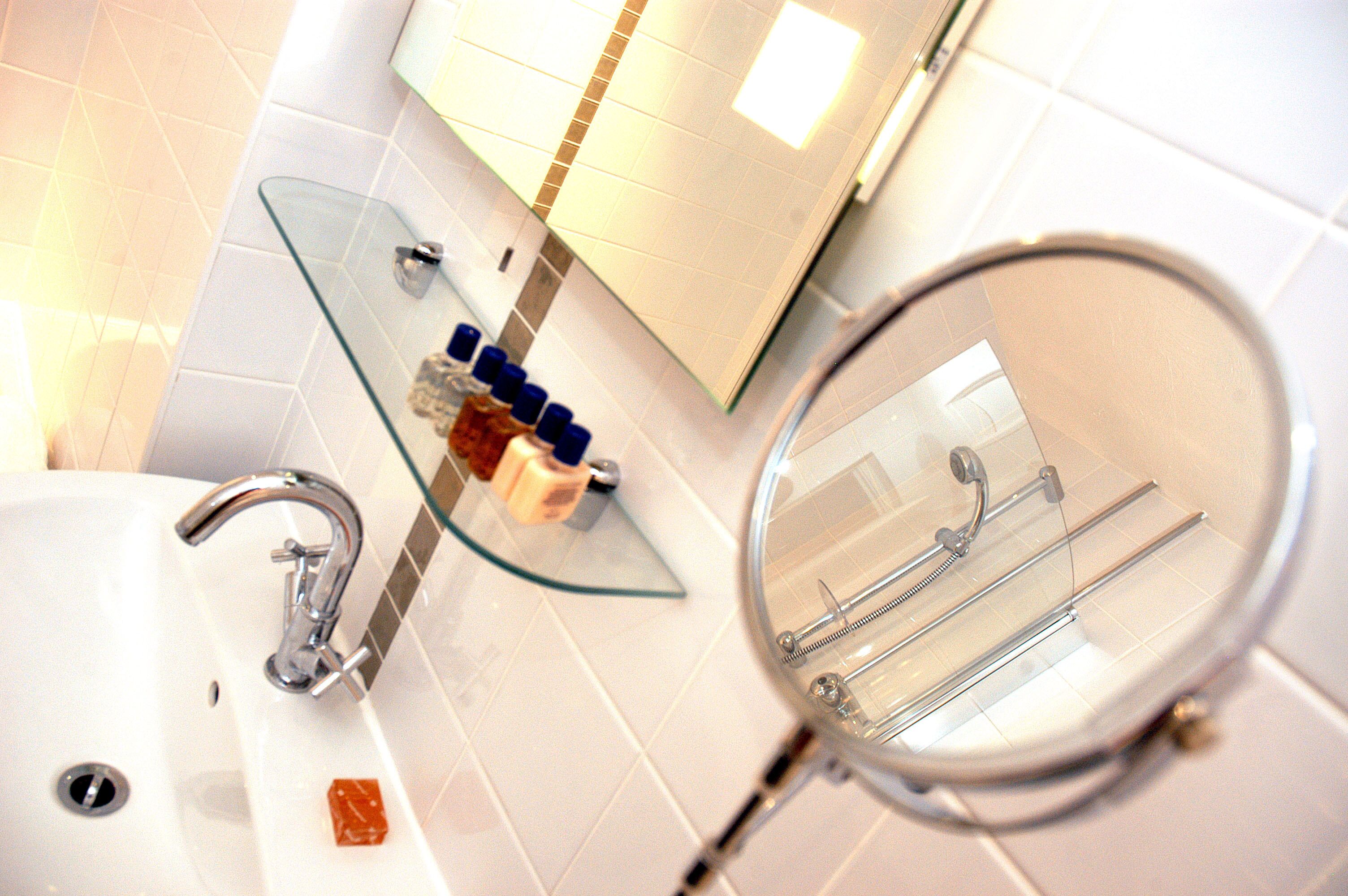 A bathroom with a glass shelf holding toiletries, a round mirror, and a white sink with a chrome faucet.