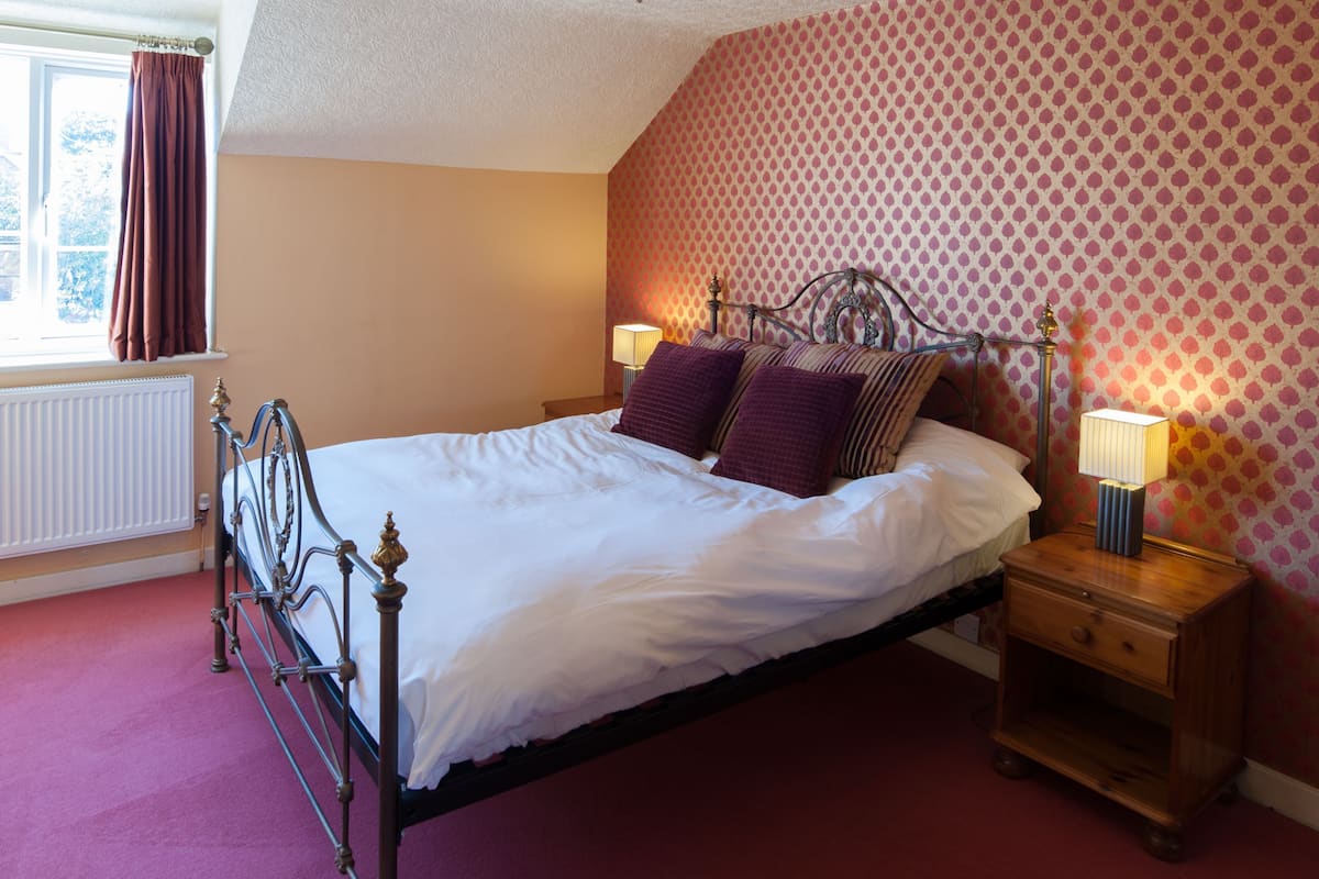 A bedroom with a bed, a nightstand, a lamp, and a window with curtains.