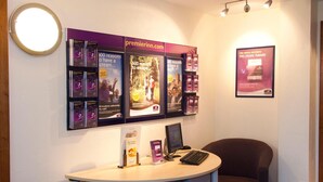 A reception desk with a computer, brochures, and a framed poster on the wall. - Premier Inn Manchester - Handforth (Wilmslow)