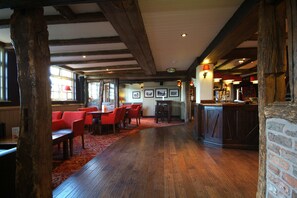 A restaurant with wooden beams, red chairs, a bar area, and a red carpet.