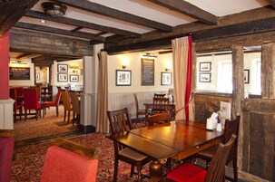 Un comedor con mesas y sillas de madera, cuadros en las paredes y una cortina roja.