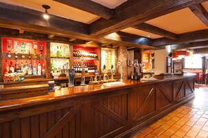 A bar with wooden beams, a variety of liquor bottles, and a counter with taps.