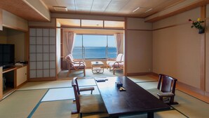 A traditional Japanese-style room with tatami flooring, a low table, two chairs, and a television. - Kameya-Rakan (Ito)