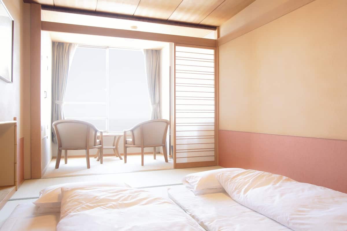 Une chambre d’hôtel avec un lit, deux chaises, une petite table et une fenêtre avec des rideaux.