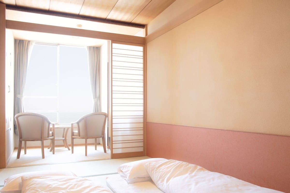 Une chambre d’hôtel avec un lit, deux chaises, une fenêtre et une porte coulissante.