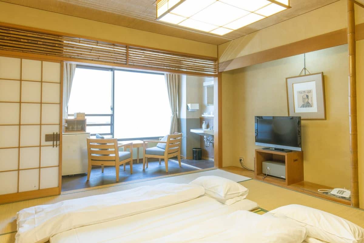 Une chambre d’hôtel comprenant un lit, une télévision, un bureau avec une chaise et une porte coulissante donnant sur un balcon.