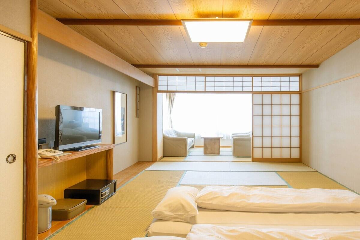 Une pièce de style japonais traditionnel, avec un sol recouvert de tatamis, un téléviseur posé sur une étagère en bois et un paravent coulissant de type shoji.