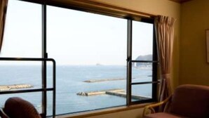 A room with a large window, a chair, a small table, and a view of the sea. - Kameya-Rakan (Ito)