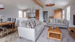 A modern living room with a grey sofa, wooden coffee table, and a dining area with a wooden table and chairs. - Roydon Marina Village (Harlow)