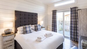 A neatly made bed with white linens and two pillows, a bedside lamp, and a nightstand with a decorative item. - Roydon Marina Village (Harlow)