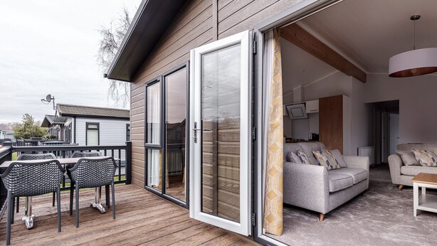 A modern outdoor deck with a wooden floor, a dining area with metal chairs, and a sofa set. - Roydon Marina Village (Harlow)