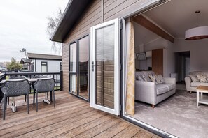 A modern outdoor deck with a wooden floor, a dining area with metal chairs, and a sofa set. - Roydon Marina Village (Harlow)