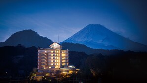 A multi-story hotel with illuminated windows, a prominent roof sign, and a view of a mountain in the background. - Izu Nagaoka Hotel Tenbo (Izunokuni)