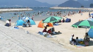 A beach with tents and umbrellas, a rocky shoreline, and mountains in the background. - Izu Nagaoka Hotel Tenbo (Izunokuni)