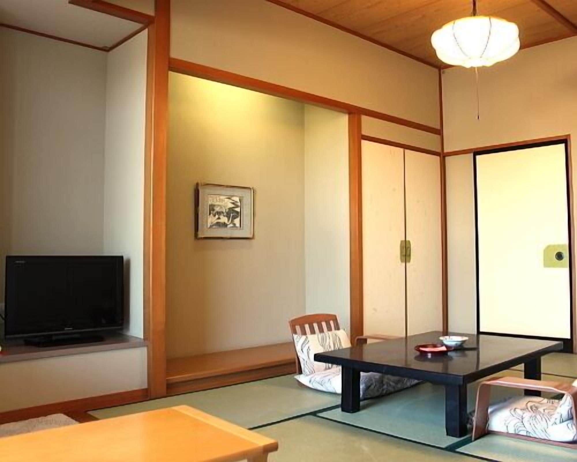A traditional Japanese room with tatami flooring, a low table, a television, and sliding doors.