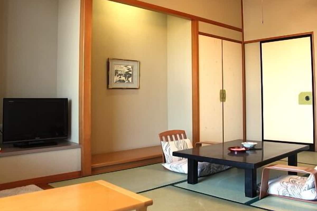 Une pièce de style japonais traditionnel, avec un sol recouvert de tatamis, une table basse, un téléviseur et des portes coulissantes.