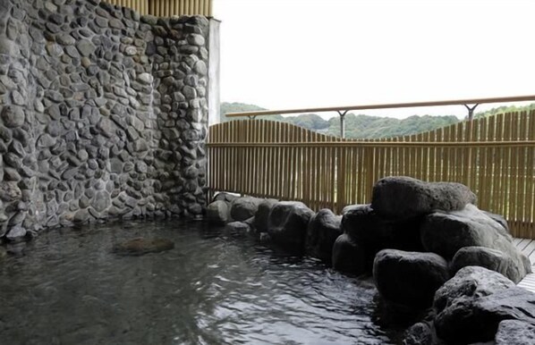 Muro de piedra y valla de madera con un elemento decorativo de agua al frente.