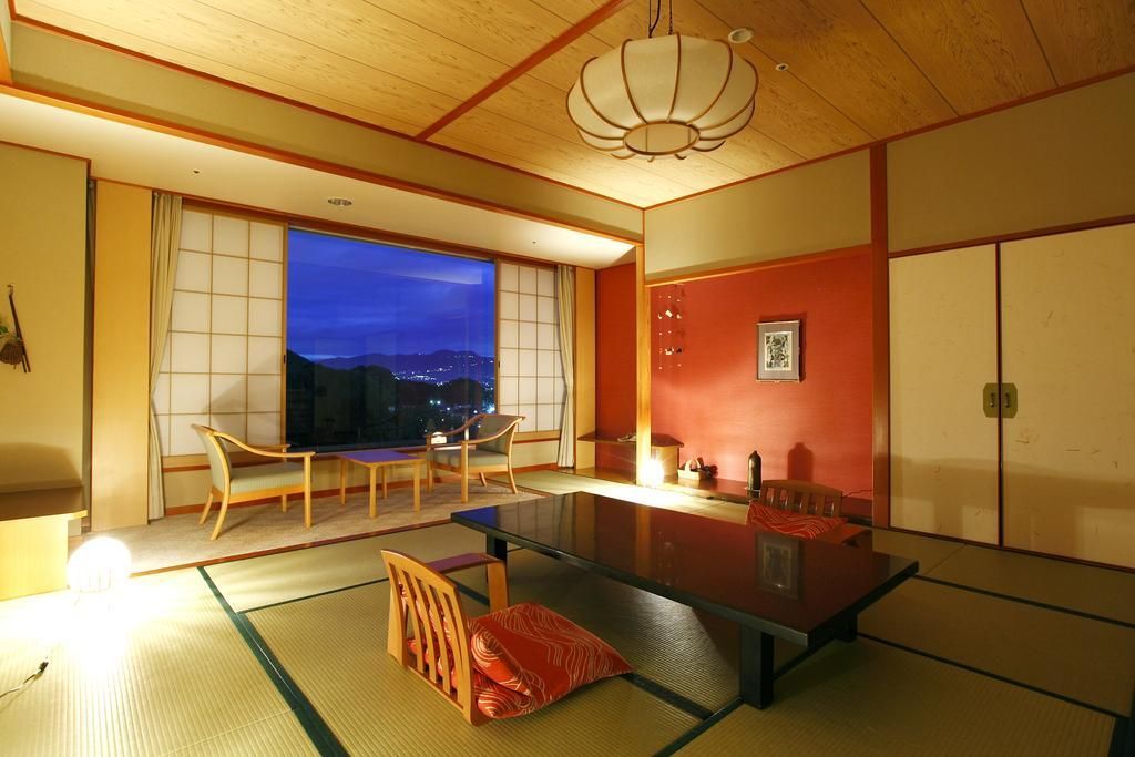 A traditional Japanese room with tatami flooring, a low table, and a view of the city at dusk.