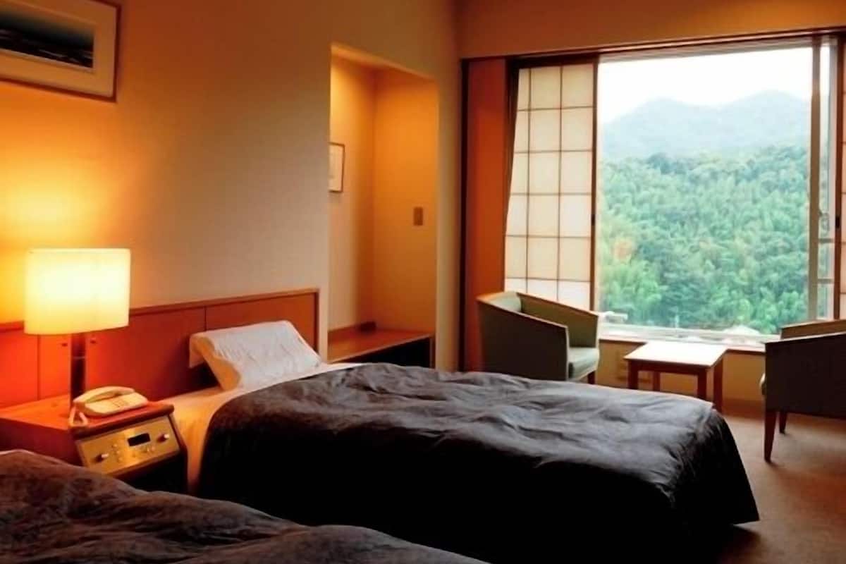 Une chambre d’hôtel avec deux lits, un bureau, une chaise et une grande fenêtre donnant sur la montagne.