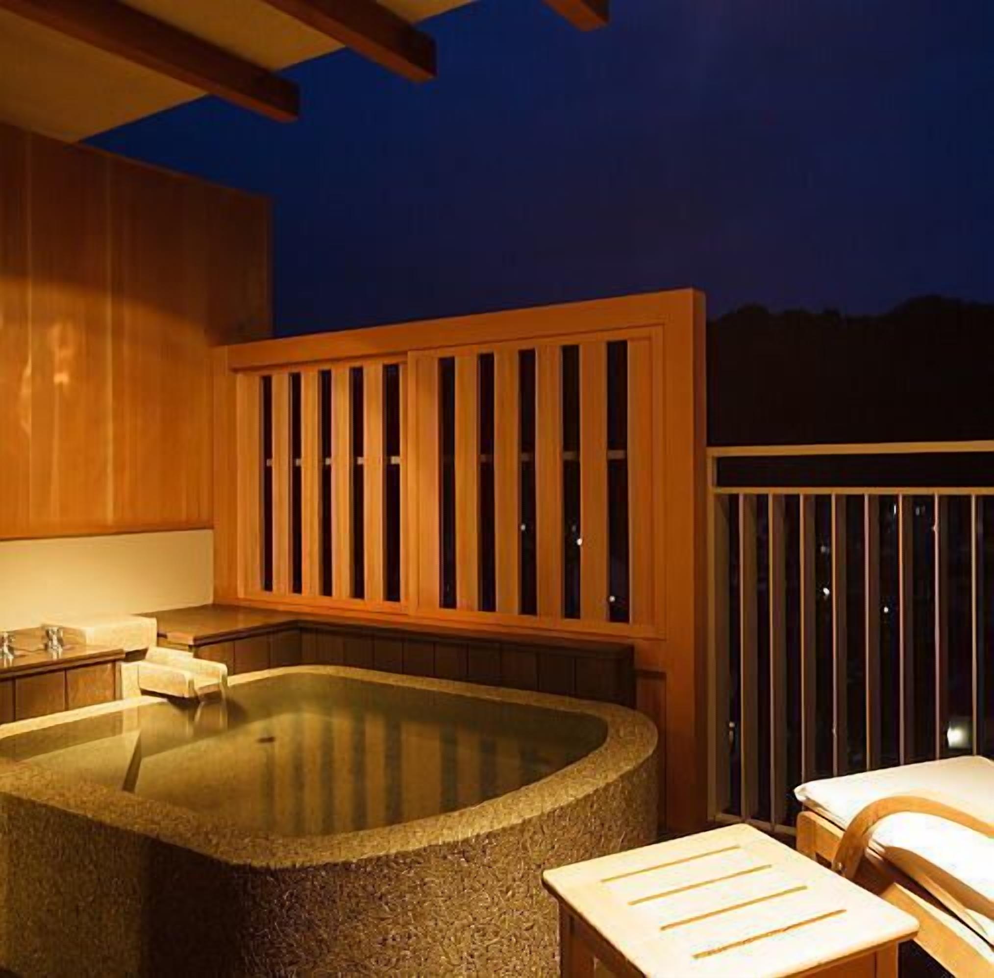 A hot tub with wooden railings, a stone basin, and a seating area with a table and chairs.