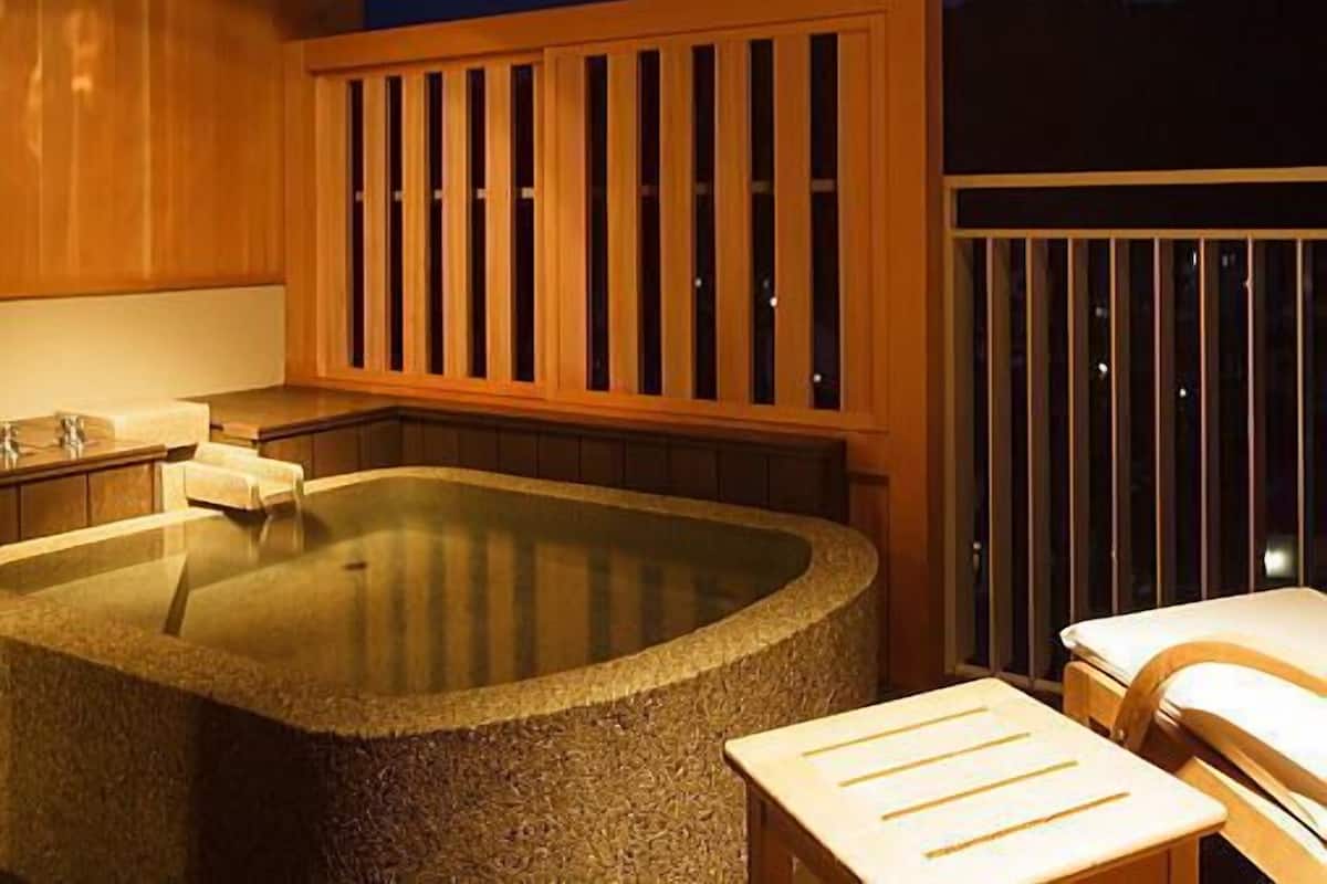 Un bain à remous doté de rampes en bois, d’un bassin en pierre et d’un espace détente avec une table et des chaises.