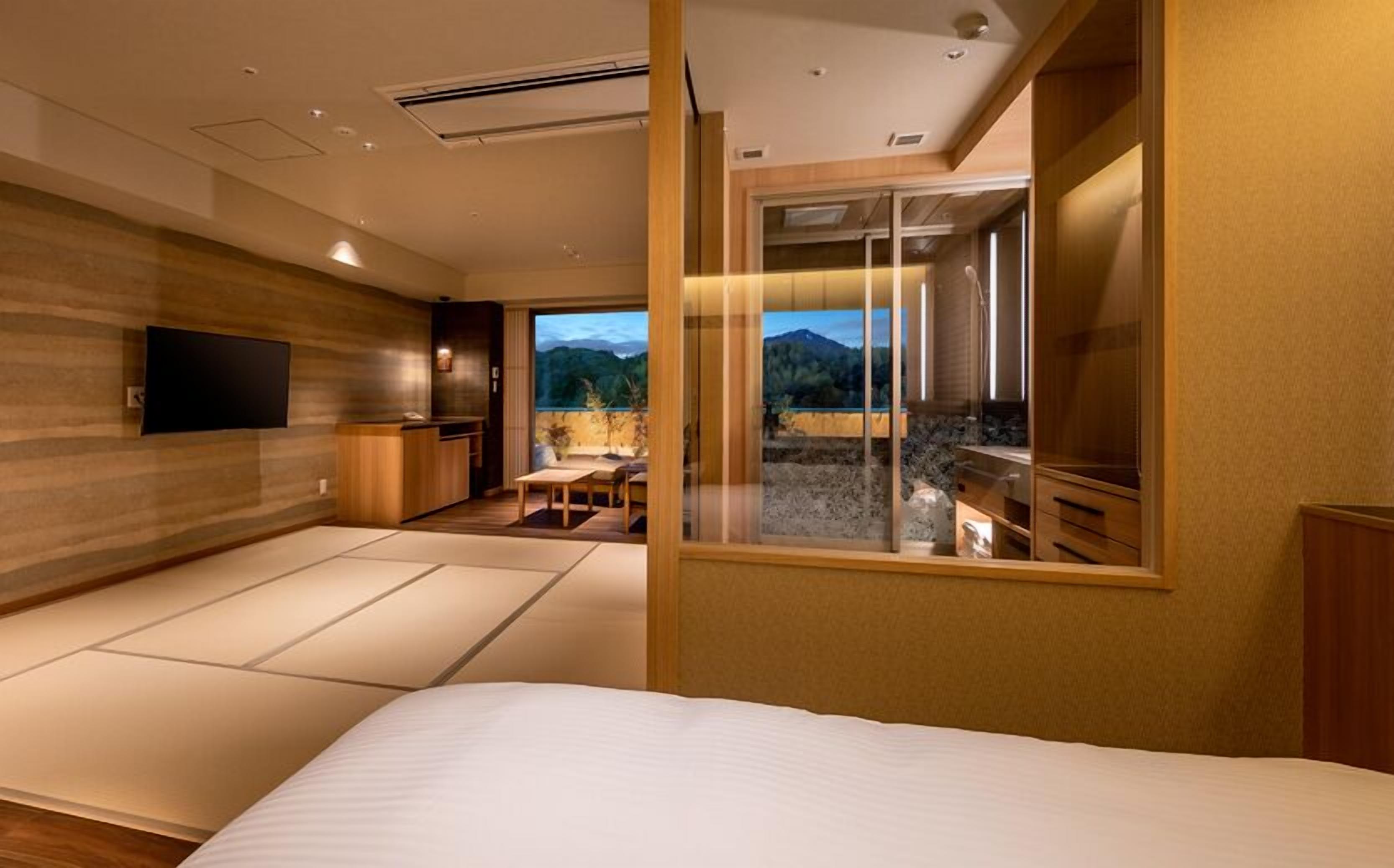 Ein modernes Hotelzimmer mit einem großen Bett, einem Fernseher, einem Essbereich und Blick auf Berge.