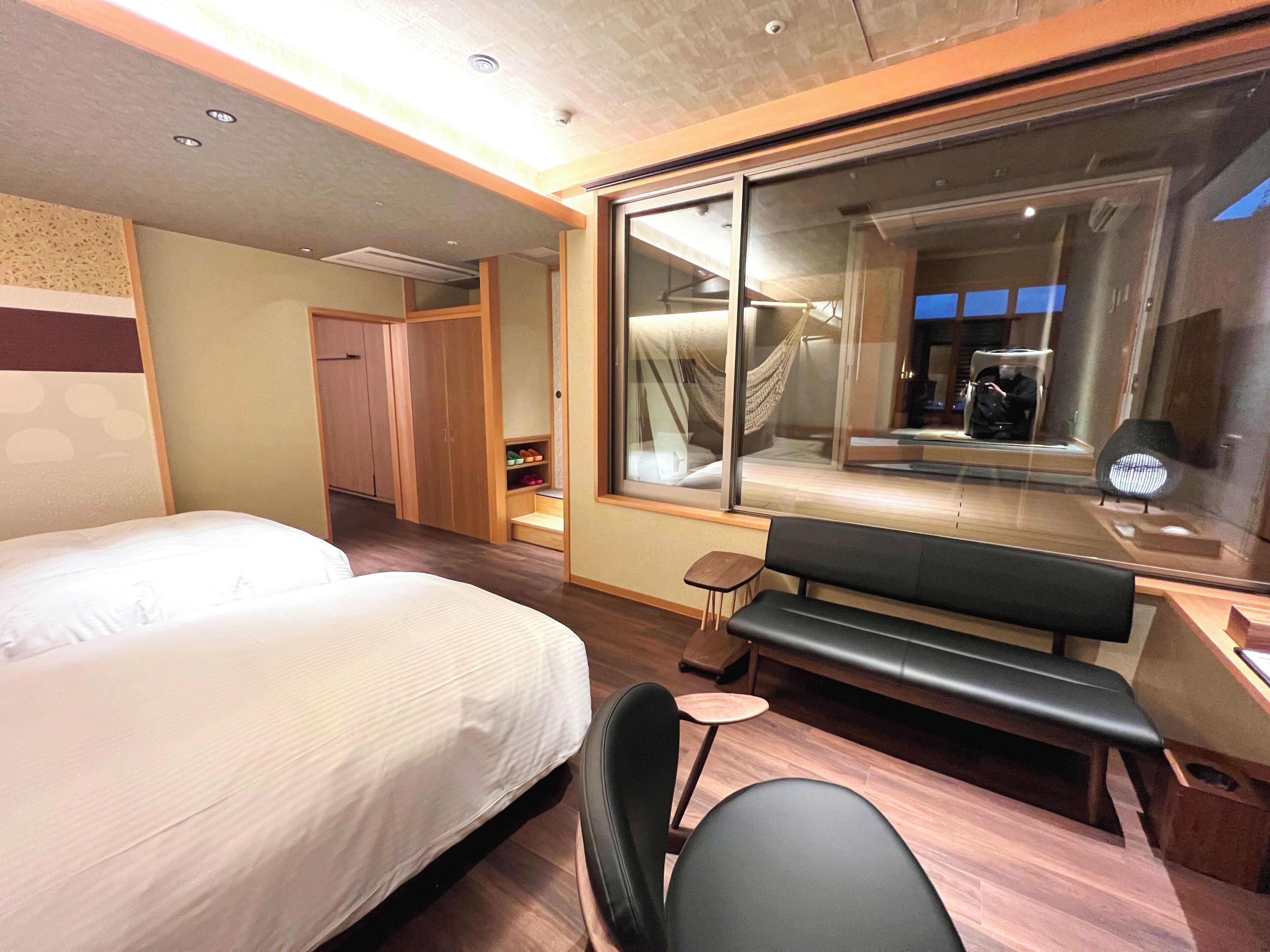 Ein Hotelzimmer mit Bett, einer Sitzbank, Schreibtisch, Stuhl, Kleiderschrank und einem großen Fenster mit Blick.