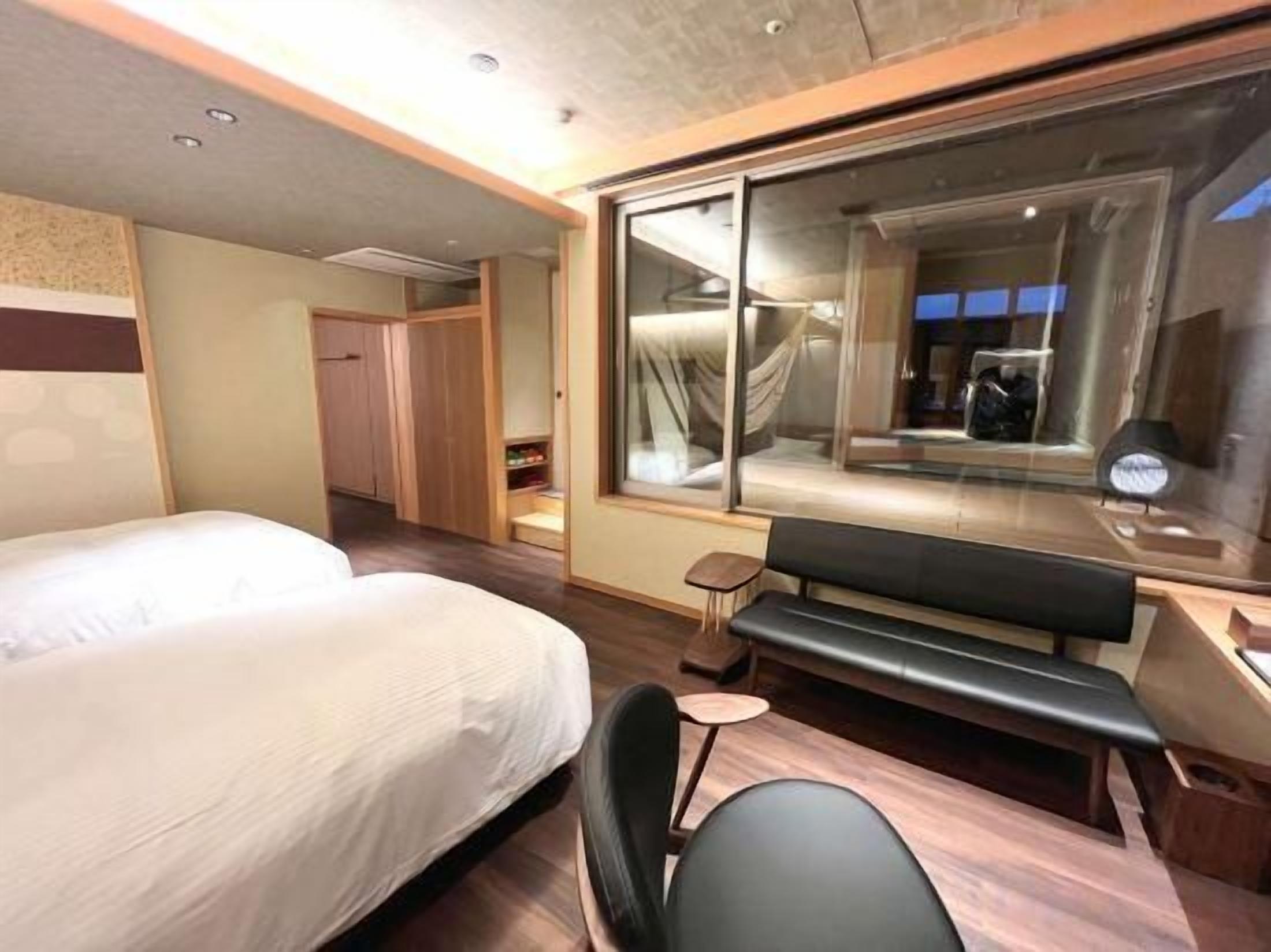 Habitación de hotel con dos camas, un banco, una mesita pequeña y un ventanal grande.