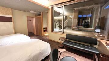 Habitación de hotel con dos camas, un banco, una mesita pequeña y un ventanal grande.