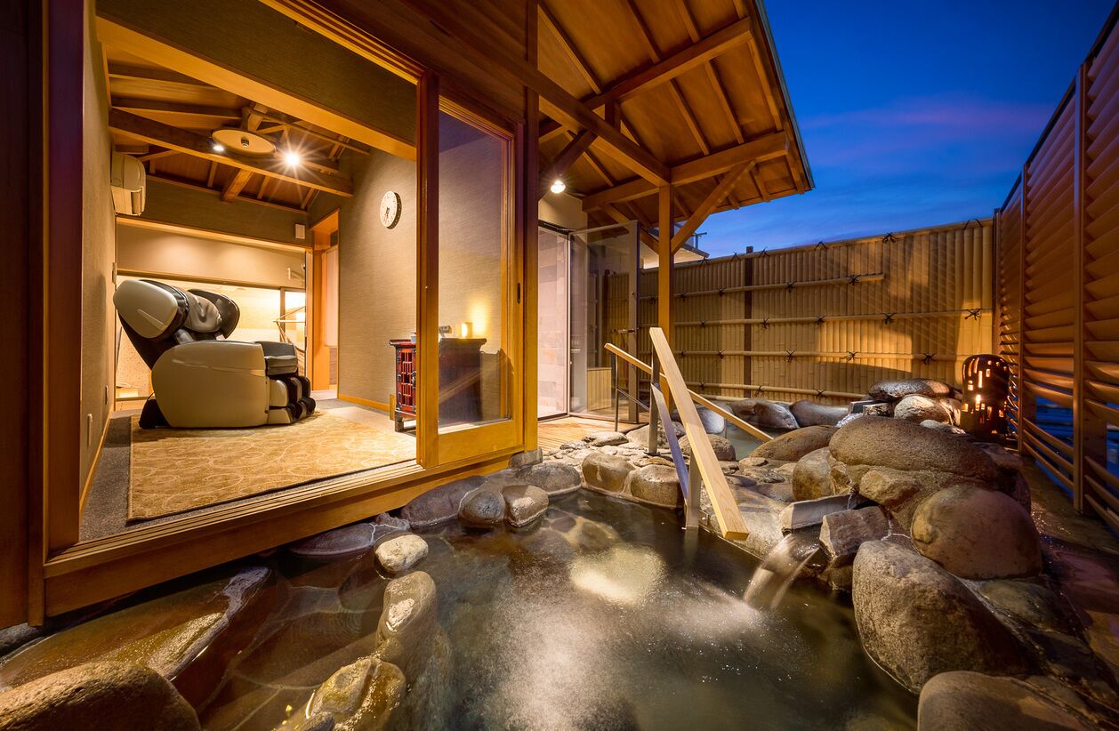 A traditional Japanese onsen with a wooden interior, a stone hot spring, and a wooden fence.