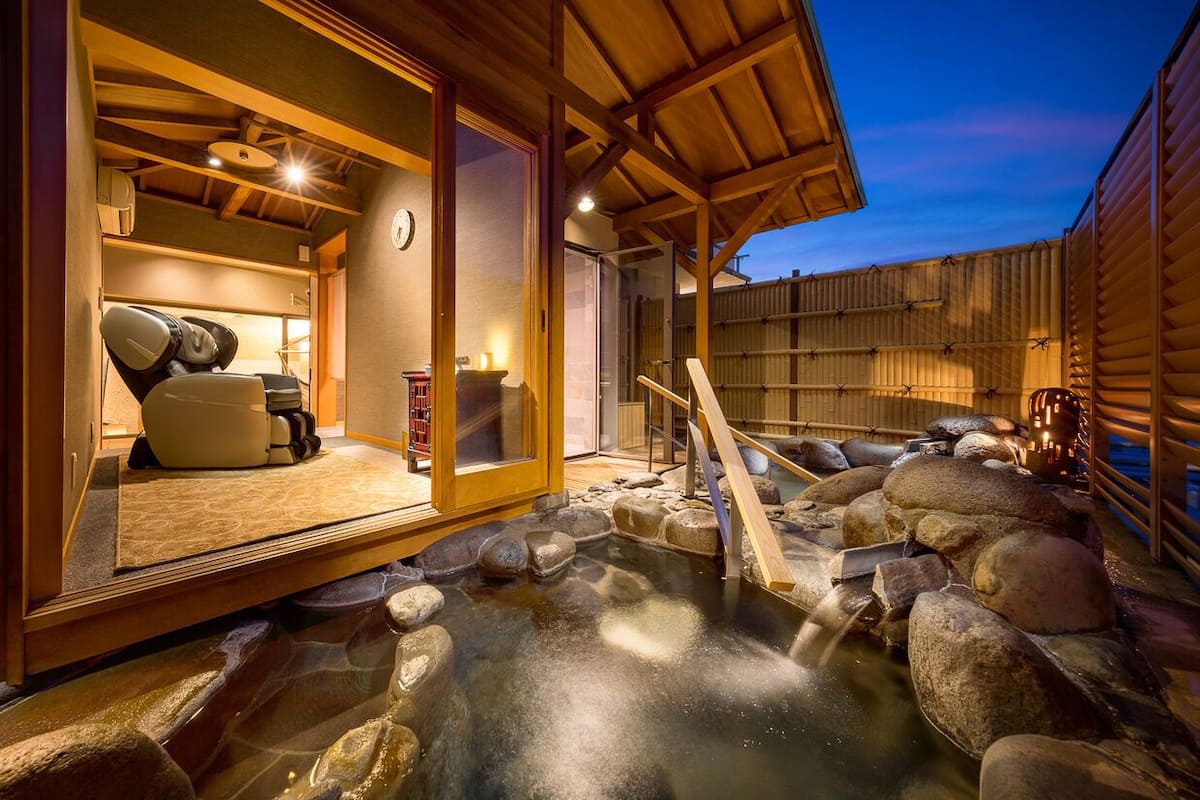 Un onsen japonais traditionnel, avec un intérieur en bois, une source d’eau chaude entourée de pierres et une clôture en bois.