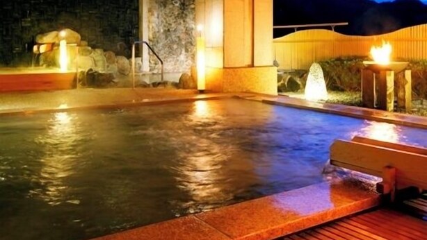 A hot spring area with stone walls, wooden benches, and a view of the mountains at dusk. - Izu Nagaoka Hotel Tenbo (Izunokuni)