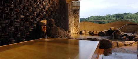 Un baño de aguas termales con un banco de madera, un muro de piedra y vistas a un bosque.
