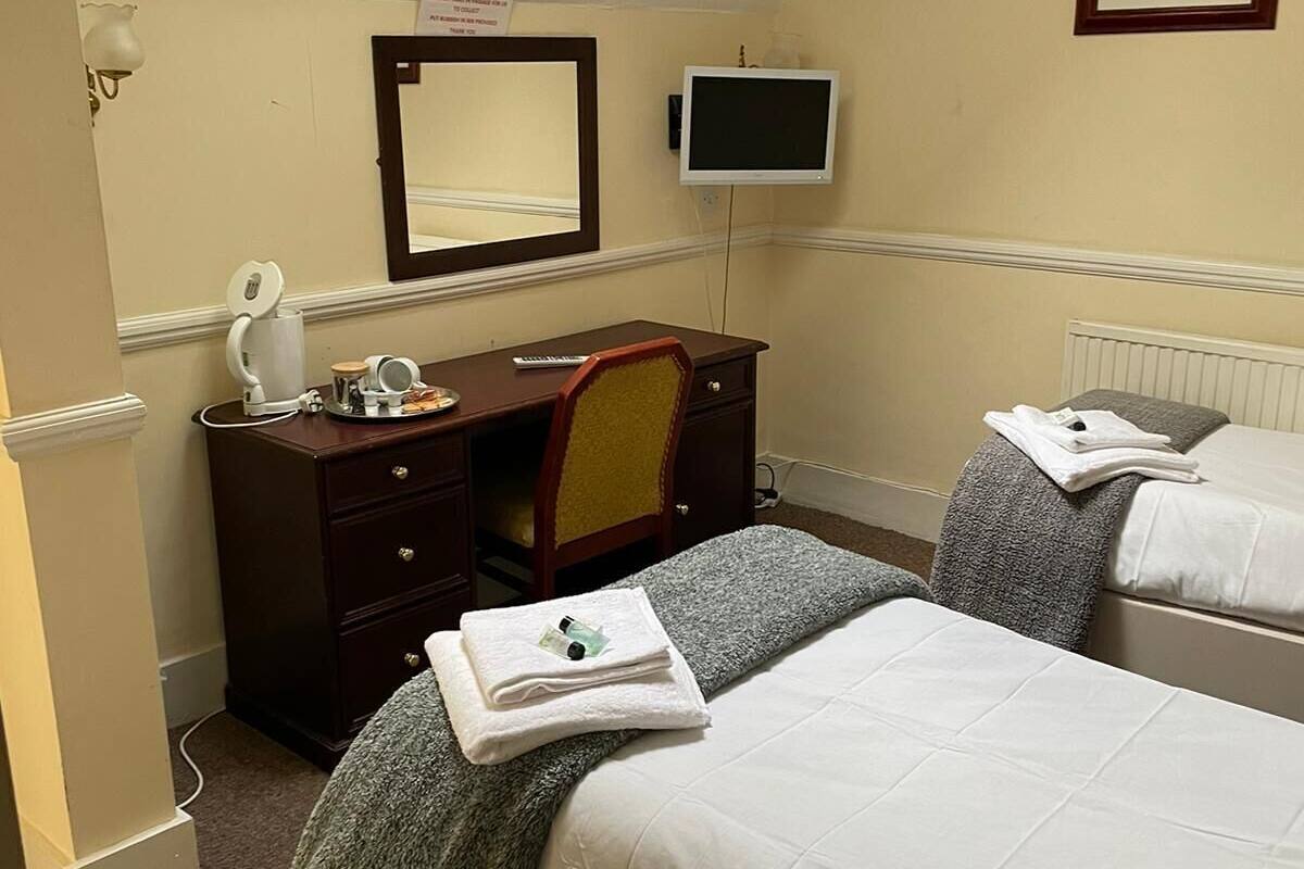 A hotel room with a bed, a desk with a chair, a television, and a mirror.