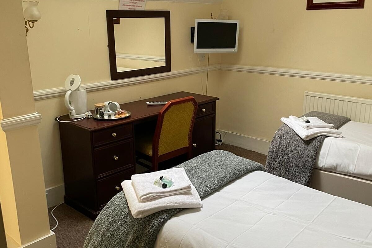 A hotel room with a bed, a desk with a chair, a television, and a mirror.