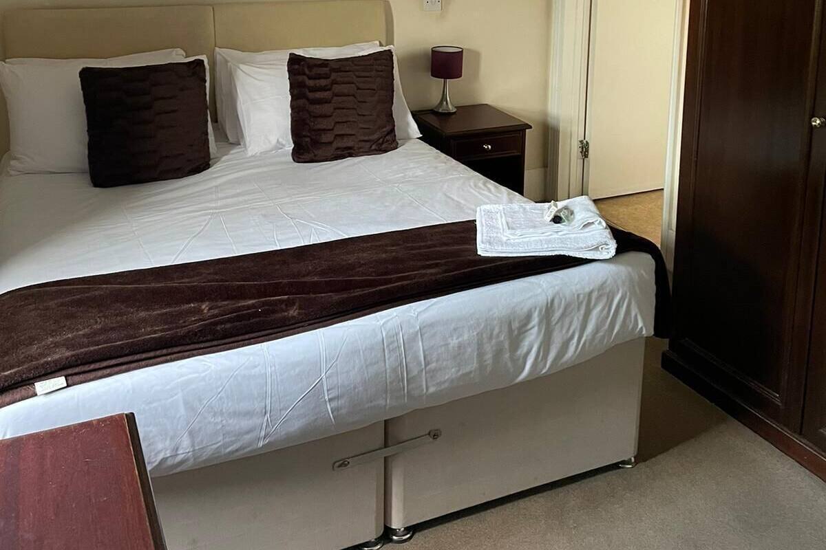 A neatly made bed with a dark headboard, a bedside lamp, and a wooden nightstand.